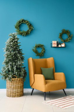 Oturma odasının içinde Noel ağacı, çelenk ve koltuk var.