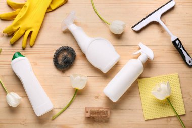 Cleaning supplies with tools and tulip flowers on light wooden background