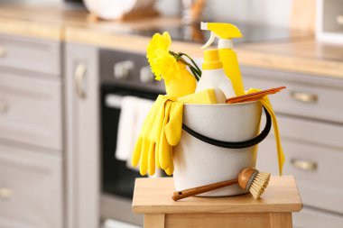 Evdeki sandalyede temizlik malzemeleri, aletler ve nergis çiçekleriyle dolu bir kova.