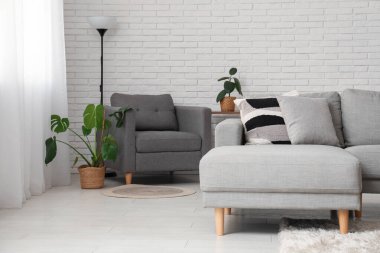 Oturma odasının içindeki beyaz tuğla duvarın yanında rahat bir kanepe ve koltuk.