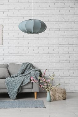 Oturma odasındaki beyaz tuğla duvarın yanında puf ve vazo açan dallarla dolu kanepe.