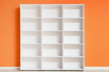Turuncu duvarın yanında boş beyaz raf ünitesi