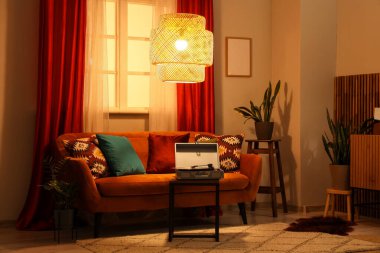 Modern dizüstü bilgisayarlı rahat bir kanepe ve oturma odasındaki kırmızı perdelerin yanında parlayan bir lamba.