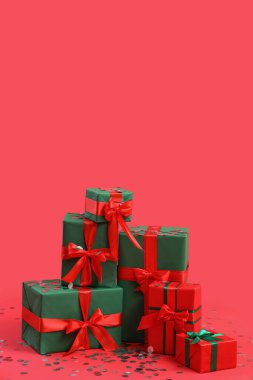Kırmızı arka planda konfeti olan Noel hediyeleri