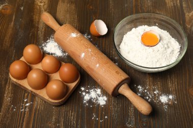 Tahta zemin üzerinde bir kase un ve yumurta ile yuvarlanan iğne.