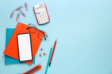 Mavi arka planda cep telefonu ve gözlüklü okul kırtasiyesi
