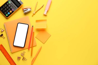 Sarı arka planda cep telefonu olan okul kırtasiyesi.