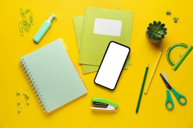 Sarı arka planda cep telefonu ve bitki örtüsü olan okul kırtasiyesi.