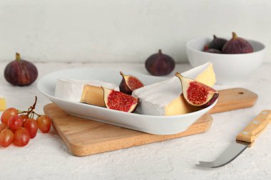 Lezzetli Camembert peyniri ve beyaz grunge arka planda taze incir parçaları, yakın plan.