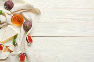 Lezzetli Camembert peyniri, taze incir ve beyaz ahşap arka planda bir kase bal içeren kompozisyon.