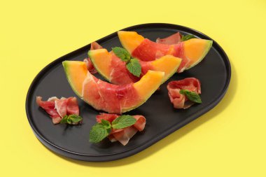 Lezzetli prosciutto ve sarı arka planda nane yapraklı taze kavun parçaları.