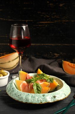 Lezzetli jambonlu taze kavun parçaları ve siyah ahşap arka planda fesleğen yaprakları.