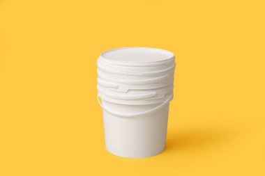 Sarı arka planda beyaz plastik boya kovaları