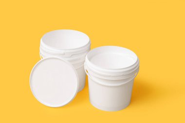 Sarı arka planda beyaz plastik boya kovaları