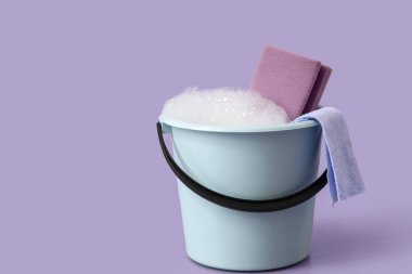 Mor arka planda köpük, sünger ve bez kaplı plastik kova.