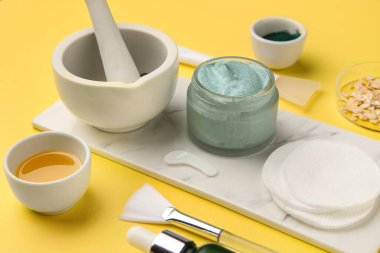 Mermer tepside bir kavanoz spirulina yüz maskesi, pamuk pedleri ve sarı arka planda havan topu, yakın plan