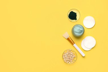 Bir kavanoz spirulina yüz maskesi ve sarı arka planda malzemeler.