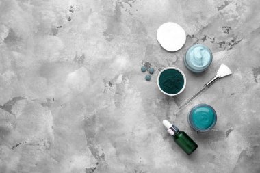 Kavanozlar dolusu spirulina yüz maskesi ve gri grunge arka planda bir şişe kozmetik ürünü.