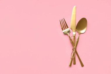 Pembe arka planda şık altın çatal bıçak takımı