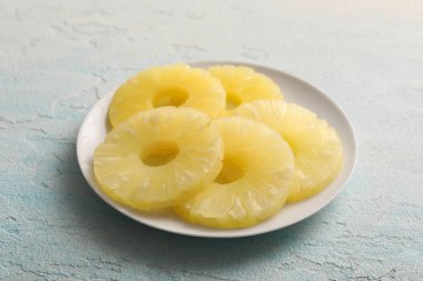 Açık mavi zemin üzerinde konserve ananas halkaları olan tabak, yakın plan.