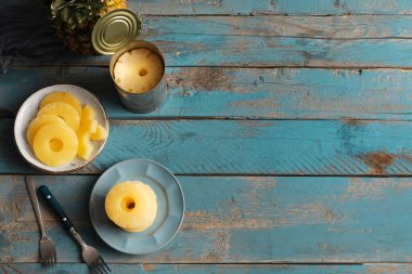 Tabaklar ve konserve ananas halkaları mavi ahşap arka planda.