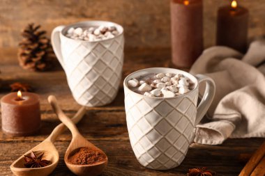 Marşmelovlu sıcak kakao bardakları ve ahşap arka planda yanan mumlar.