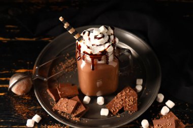 Mason kavanozu kremalı sıcak kakao içeceği ve siyah ahşap arka planda lokum.