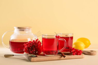 Sarı arka planda limonlu cam bardaklar ve bir çaydanlık sıcak viburnum çayı.