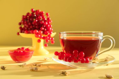 Sarı arka planda bir bardak sıcak viburnum çayı ve dut.