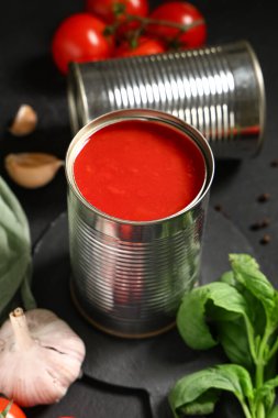 Siyah arka planda sarımsak ve fesleğen yapraklı konserve domates ezmesi, yakın plan.