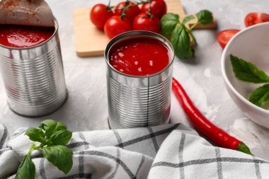 Fesleğen yapraklı teneke kutu domates ezmesi ve gri arka planda kırmızı biber. Yakın plan.