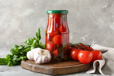 Gri arka planda sarımsak ve fesleğen yapraklı bir kavanoz lezzetli domates.