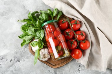 Gri arka planda sarımsak ve fesleğen yapraklı bir kavanoz lezzetli domates.