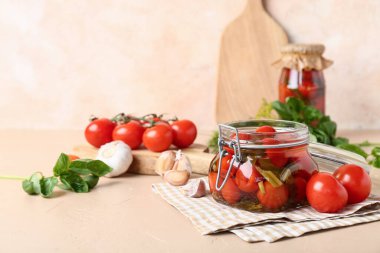 Bej arka planda sarımsaklı ve fesleğenli konserve domates kavanozu.