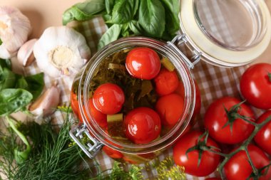 Bej arka planda sarımsaklı, dereotlu ve fesleğenli bir kavanoz lezzetli domates.