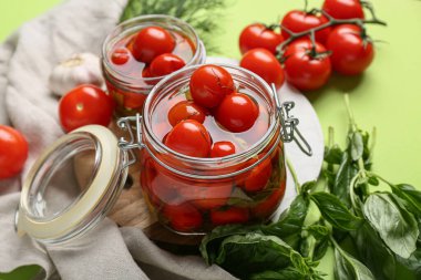 Kavanozlar dolusu lezzetli domates ve yeşil arka planda fesleğen yaprakları, yakın plan.