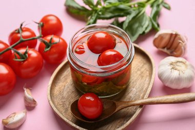 Pembe arka planda sarımsak ve fesleğen yapraklı bir kavanoz lezzetli domates, yakın plan.