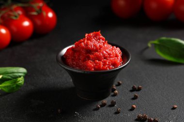 Biberli bir kase lezzetli domates ezmesi ve siyah arka planda fesleğen yaprağı. Yakın plan.