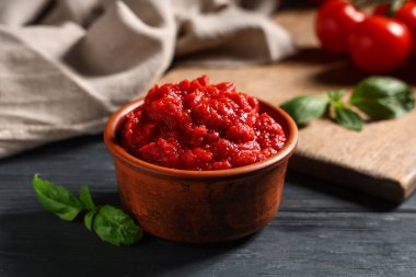 Siyah ahşap arka planda fesleğen yapraklı bir kase lezzetli domates ezmesi, yakın plan.