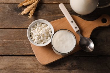 Tahta zemin üzerinde buğday ve bir kase süzme peynirli bir bardak taze kefir.