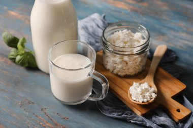 Bir bardak taze kefir fesleğen yaprağı ve mavi ahşap arka planda bir kavanoz süzme peynir.