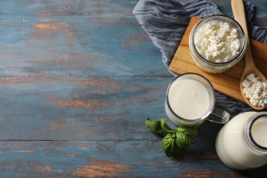 Bir bardak taze kefir fesleğen yaprağı ve mavi ahşap arka planda bir kavanoz süzme peynir.