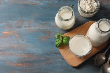 Fesleğen yapraklı bir bardak taze kefir ve mavi ahşap arka planda bir kavanoz süzme peynir.