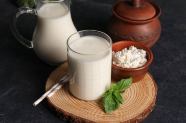 Fesleğen yapraklı bir bardak taze kefir ve siyah arka planda bir kase süzme peynir, yakın plan.