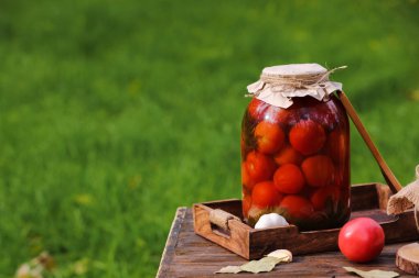 Sarımsaklı konserve domates kavanozu ve dışarıdaki ahşap masada defne yaprakları.