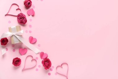 Gül çiçeklerinden, kağıt kalplerden ve pembe arka planda hediye kutusundan yapılmış çerçeve