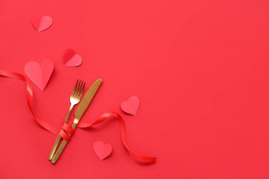 Kırmızı arka planda çatal bıçak, kurdele ve kağıt kalplerle kompozisyon. Sevgililer Günü kutlaması