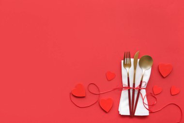 Kırmızı arka planda çatal bıçak, peçete ve dekoratif kalplerle kompozisyon. Sevgililer Günü kutlaması
