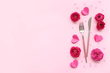 Çatal bıçak takımları, kağıt kalpler, gül çiçekleri ve pembe arkaplanlı boncuklar. Sevgililer Günü kutlaması