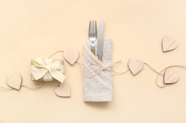 Çatal bıçaklı kompozisyon, hediye kutusu ve bej arka planda tahta kalpler. Sevgililer Günü kutlaması